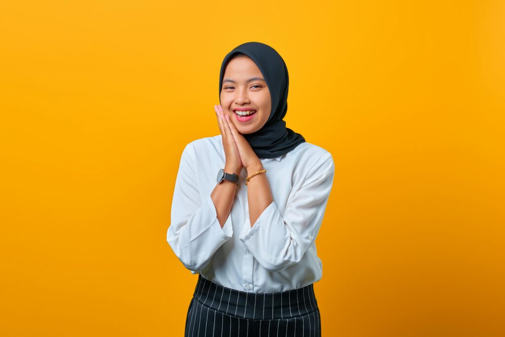 Cheerful Muslim woman in a hijab smiling against a vibrant yellow backdrop.