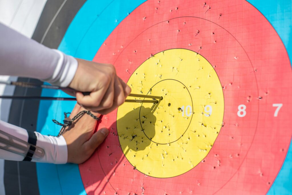 An archer retrieves arrows from a colorful archery target during a sunny day outdoors.